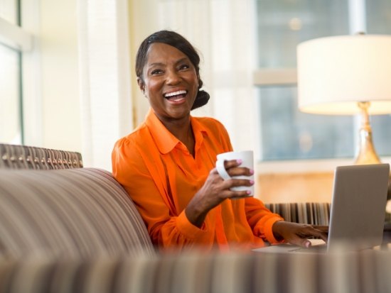 Woman in orange shirt sitting on couch with coffee cup