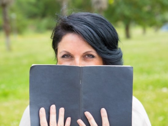 Woman sitting outside peeking over a book