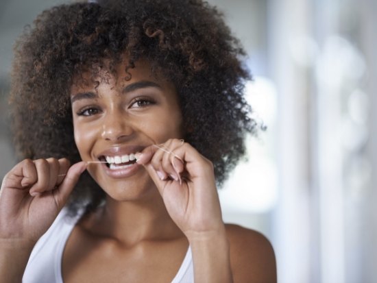 Woman with a white shirt flossing her teeth