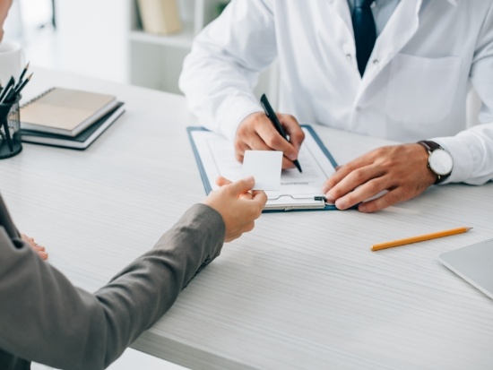 Dentist writing on a clipboard while patient hands them a slip of paper