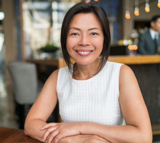 Woman in white sleeveless shirt sitting at table and smiling