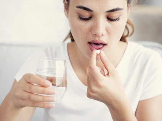 Woman holding glass of water about to take a pill