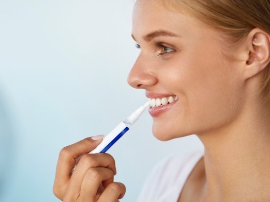 Woman smiling and applying whitening gel to her teeth