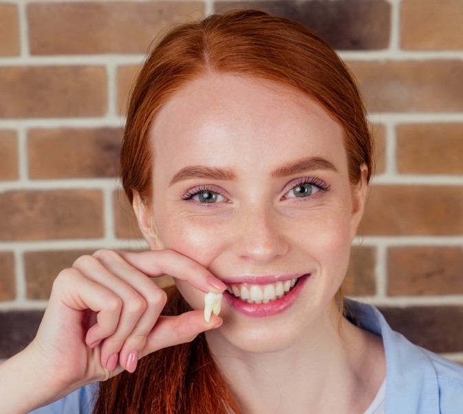 Red haired woman smiling and holding up a tooth